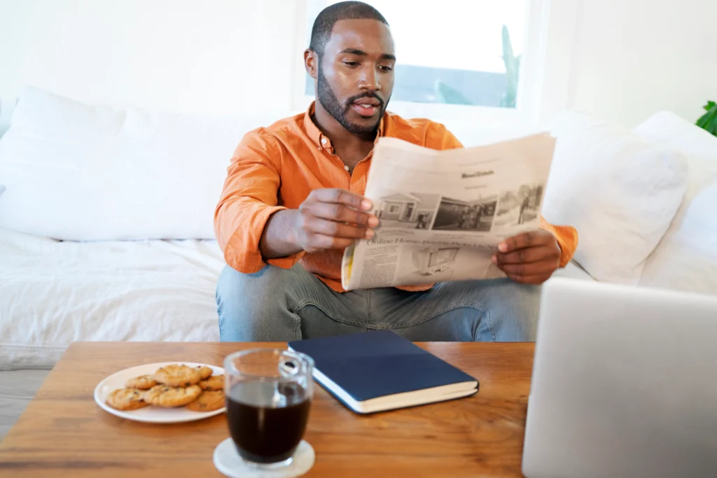 young man reading newspaper home while having coffee